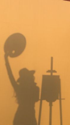 the shadow of a person holding up a disc in front of a painting easel