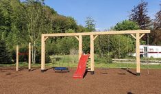 a wooden swing set with a red slide in the middle and a blue trampoline on the other side