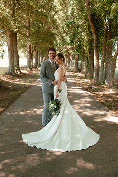 a bride and groom standing in the middle of a tree lined path