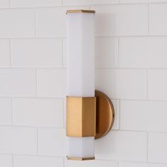 a gold and white light fixture on a wall in a room with white brick walls