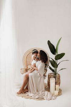 two women sitting on a wicker chair with their arms around each other and one holding the baby