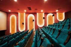 an auditorium with rows of blue seats in front of a projector screen and lights on the wall