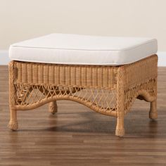 a wicker foot stool with white cushion on wooden floor in front of beige wall