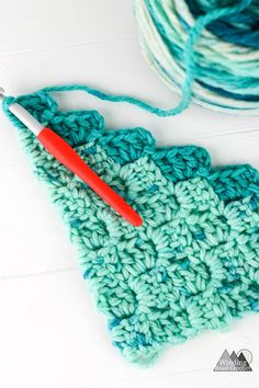 the crochet is next to a ball of yarn and a red handled knitting needle