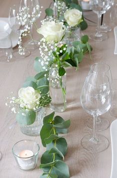 a long table with white flowers and greenery in vases on top of it