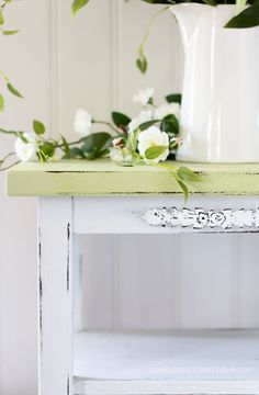 white flowers and greenery are sitting on an old wooden table in front of a white vase