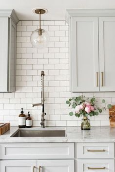 a white kitchen with marble counter tops and brass pulls on the faucet above the sink