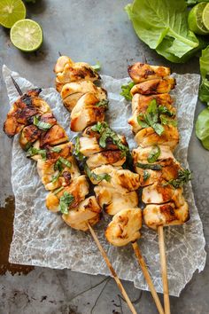 grilled chicken skewers with basil and limes on a piece of parchment paper