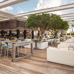 an outdoor dining area with tables, chairs and couches on wooden flooring next to trees