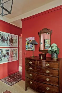 a bedroom with red walls and pictures hanging on the wall, along with a chest of drawers