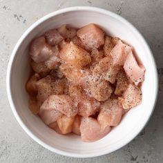 a white bowl filled with meat and seasoning sitting on top of a gray counter