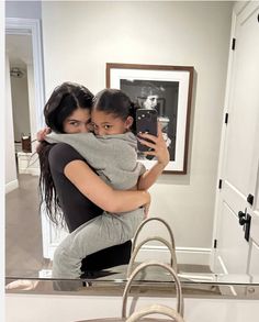 a woman taking a selfie in front of a mirror with her daughter hugging her