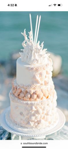 a three tiered white wedding cake sitting on top of a table next to the ocean