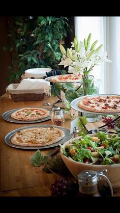 a wooden table topped with lots of pizzas next to a vase filled with flowers