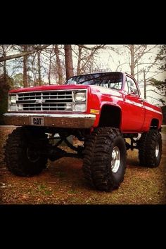 a red truck with big tires parked in the woods