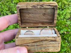 someone is holding their wedding rings in a wooden box that has sand on the inside