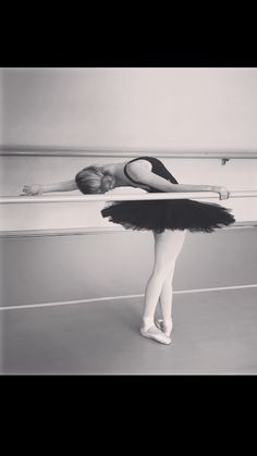 a young ballerina in black and white is leaning on the bar with her arms behind her head