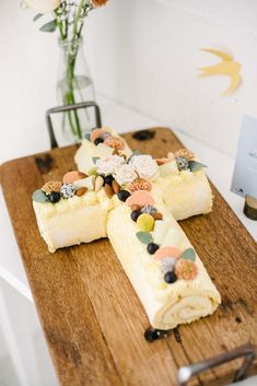 a wooden cutting board topped with two pieces of cake next to a vase filled with flowers