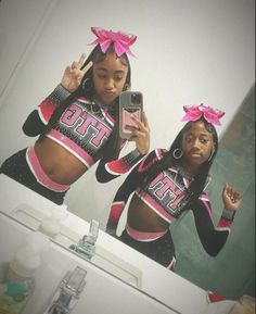 two women in cheerleader outfits are looking at their cell phones while standing in front of a mirror