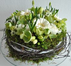 an arrangement of white flowers and greenery in a glass bowl on a table top