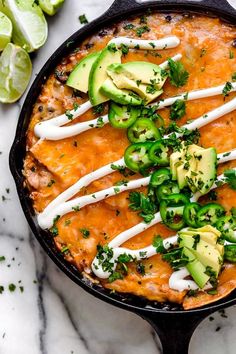 an enchilada dish in a cast iron skillet with avocado and sour cream on top