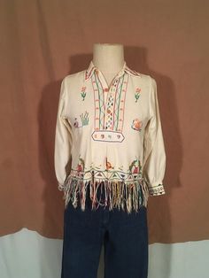 "1949 handmade souvenir blouse one of a kind pull over collared button up neck fringe hem cross stitch embroidered flowers, birds, people, elephants, bunnies good vintage condition, light wear cotton measures, lying flat, shoulder-13 1/2\" chest-18 1/2\" sleeve-18 1/2\" length-18 1/2\" length w/fringe-23\"" Vintage Cream Cotton Top, Vintage Handmade Tops For Spring, Vintage Handmade Spring Tops, Traditional Cream Cotton Top, Vintage Embroidered Tops For Fall, Vintage Embroidered Multicolor Blouse, Traditional Cream Long Sleeve Top, Traditional Long Sleeve Cream Top, Cream Cotton Tops For Festival