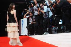 a woman in a black and white dress standing on a red carpet with cameras around her