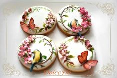 four decorated cookies sitting on top of a white plate with pink flowers and birds painted on them