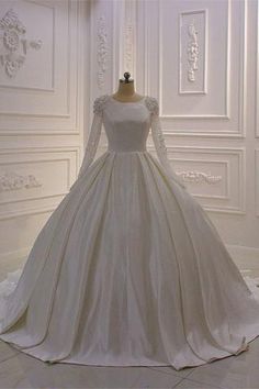 a white wedding dress with long sleeves and laces on the neckline is displayed in front of a wall