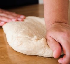 a person kneading dough on top of a wooden table