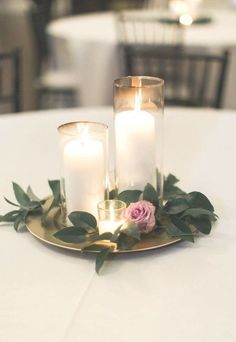 three candles are sitting on a gold plate with greenery and pink roses in it