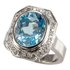 Centering an Oval 8.10 Carat Blue Topaz surrounded by twenty-four round cut diamonds; approx .24tctw; beautifully hand crafted in 18k white gold mounting; Ring size: 7.25. We offer complimentary ring re-sizing. (14mm x 12mm x 6.5mm). A Chic and Show Stopping complement to your outfit! Rings Solitaire, Sapphire Cocktail Ring, Diamond Gold Ring, Solitaire Rings, Unique Diamond Rings, Gold Statement Ring, White Gold Set, Semi Precious Jewelry, Diamond Cocktail Rings