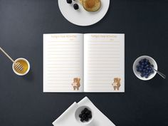 an open recipe book sitting on top of a table next to plates of fruit and pancakes