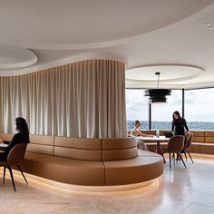 two women sitting at tables in a restaurant with large windows looking out on the ocean