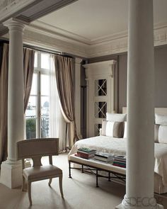 a white bed sitting next to a window in a room with curtains on the windowsill