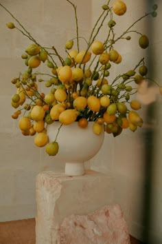 a white vase filled with yellow flowers on top of a stone block next to a wall