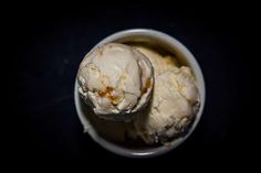 two scoops of ice cream in a white bowl on a black surface with dark background