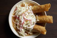 some food in a white bowl on a wooden table with chopsticks and cole slaw