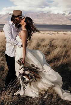 a bride and groom kissing in a field with mountains in the background