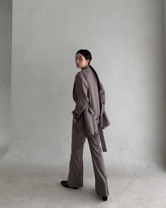 a woman standing in an empty room with her back to the camera, wearing a gray suit and black shoes