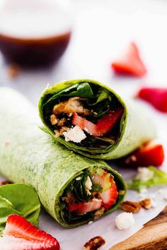 two wraps with strawberries and spinach are on a cutting board next to sliced strawberries