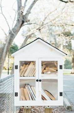 a white book case sitting on top of a wooden post next to a tree and fence