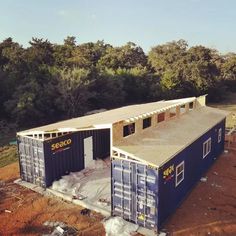 two shipping containers are being built on top of the ground in front of some trees