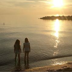 two girls standing in the water watching the sun set