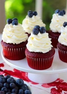 red velvet cupcakes with white frosting and blueberries on a cake plate