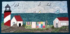 a quilted wall hanging with a lighthouse and sailboats on the water in front of a cloudy sky