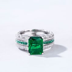 an emerald and white gold ring set with diamonds on the sides, in front of a white background