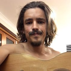 a man with long hair and a mustache holding a guitar in his right hand while looking at the camera