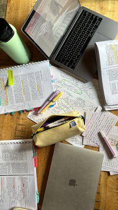 an open laptop computer sitting on top of a wooden table next to papers and pens