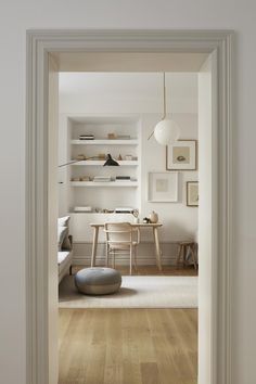 an open door leading to a living room with white walls and wooden floors, along with shelves on the wall